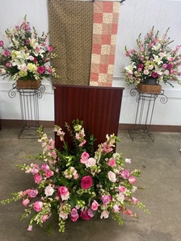 Floral arrangement in front of a podium with decorative panels, flanked by additional floral displays.