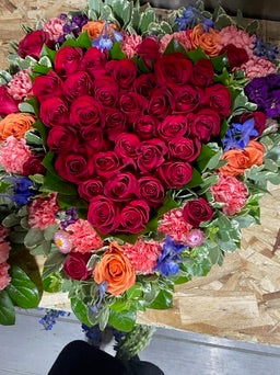 Heart-shaped arrangement of red and pink roses with colorful flowers on a wooden surface.