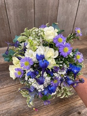 Bouquet of flowers with blue, purple, and white colors on a wooden surface.