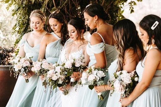 Group of women in light blue dresses holding floral bouquets outdoors.