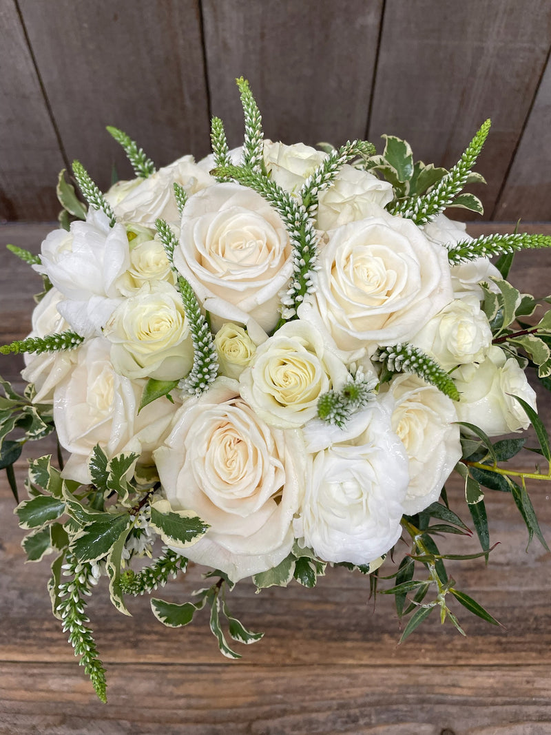 Bouquet of white and light green roses with greenery on a wooden background