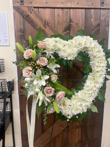 Heart-shaped floral arrangement with white and pink flowers against a wooden background
