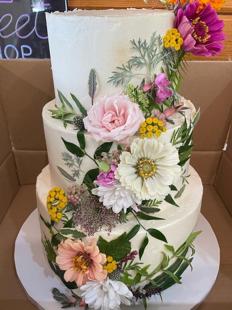 Three-tiered wedding cake decorated with flowers in a cardboard box.