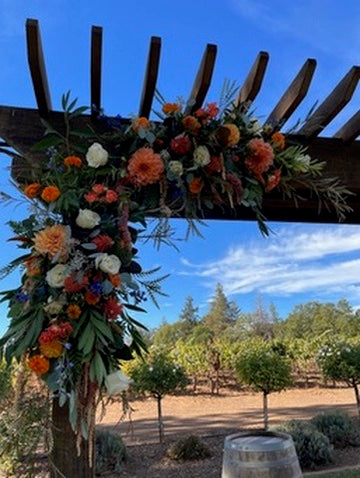 Decorative floral arch with colorful flowers against a blue sky and landscape.