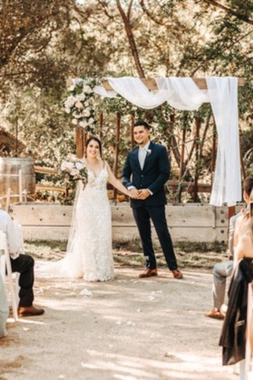 Wedding ceremony with a couple standing under a decorated archway in a natural setting.