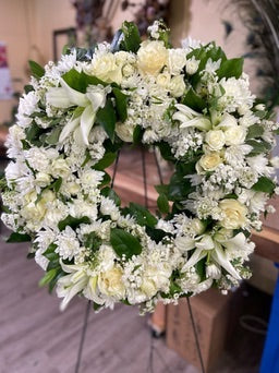Floral wreath made of white flowers and greenery on a wooden surface.