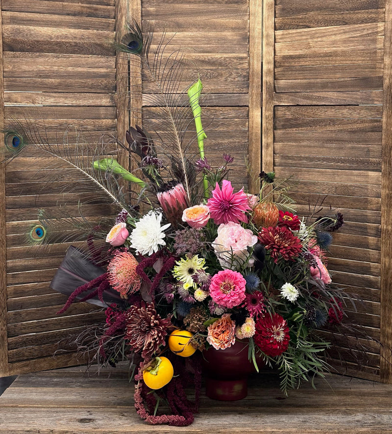 Colorful floral arrangement with peacock feathers against a wooden background