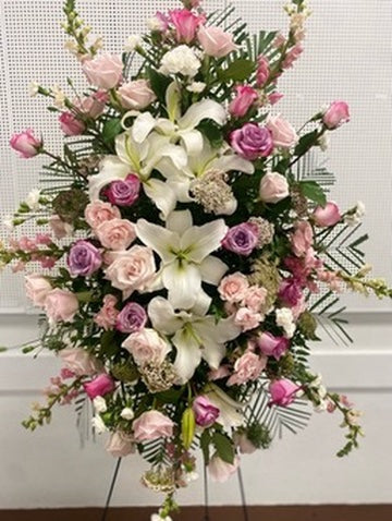 Floral arrangement with white lilies, pink roses, and greenery on a stand.