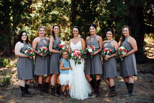 Group of women in gray dresses with floral bouquets standing outdoors.