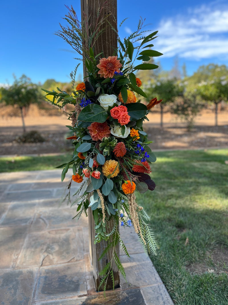Decorative floral arrangement on a wooden post with a garden background