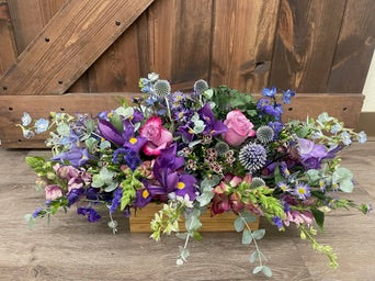 Colorful floral arrangement in a wooden box on a wooden surface with a wooden background.