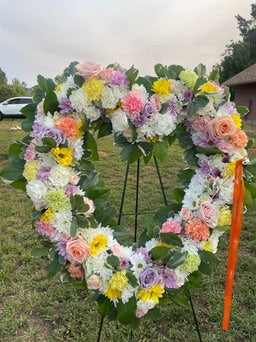 Heart-shaped floral arrangement with colorful flowers on a stand outdoors.
