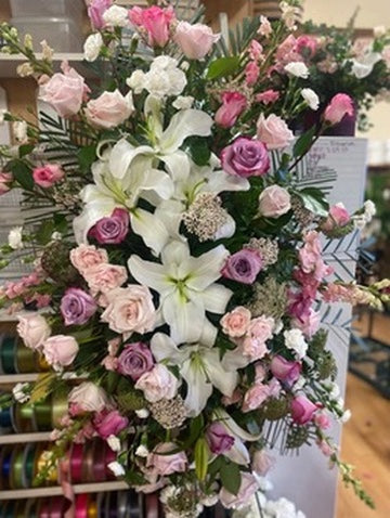 Bouquet of flowers with white lilies, pink and purple roses, and greenery in a store setting.