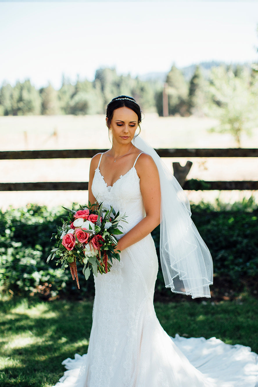 Bride in a white wedding dress holding a bouquet of flowers outdoors.