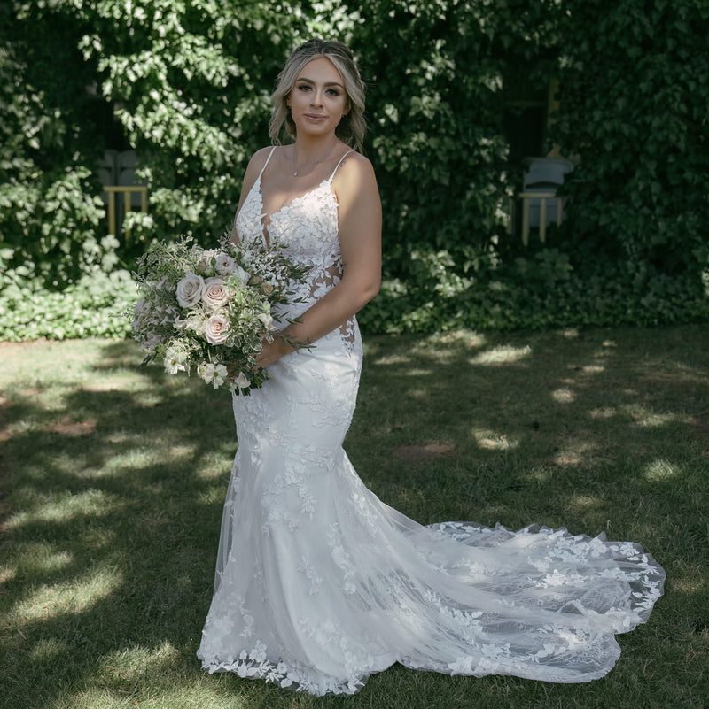 Bride in a white lace wedding dress holding a bouquet in a garden setting